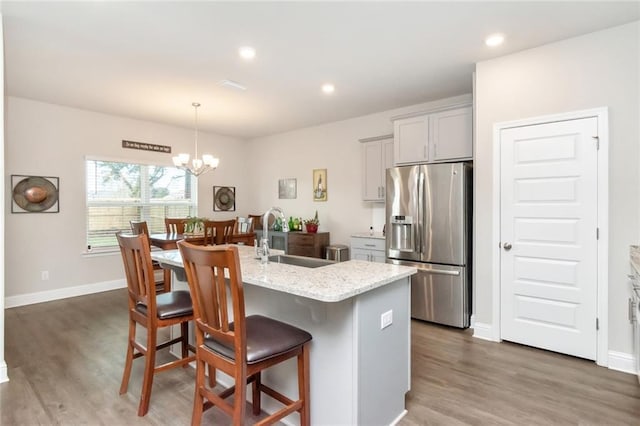 kitchen with sink, stainless steel fridge with ice dispenser, an island with sink, a chandelier, and a breakfast bar