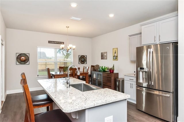 kitchen featuring light stone countertops, stainless steel fridge, a center island with sink, and sink