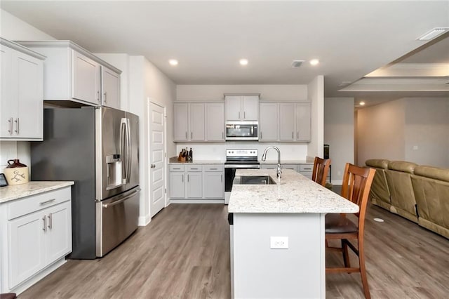 kitchen with appliances with stainless steel finishes, a kitchen breakfast bar, light stone counters, light hardwood / wood-style floors, and an island with sink