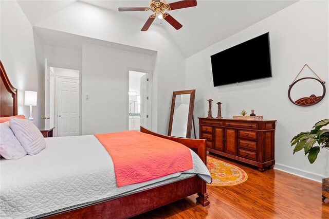 bedroom with a ceiling fan, wood finished floors, baseboards, vaulted ceiling, and connected bathroom