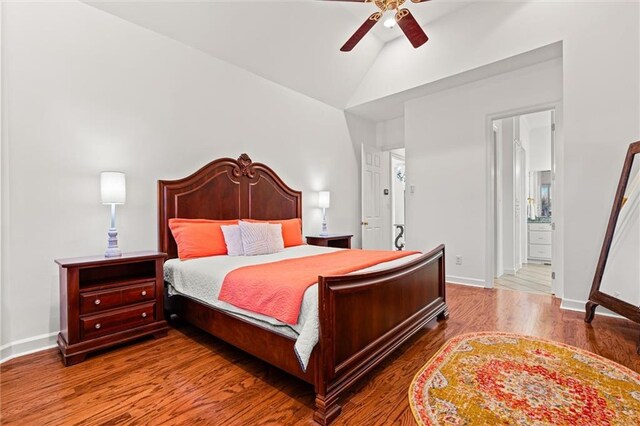 bedroom featuring wood finished floors, baseboards, a ceiling fan, ensuite bath, and vaulted ceiling