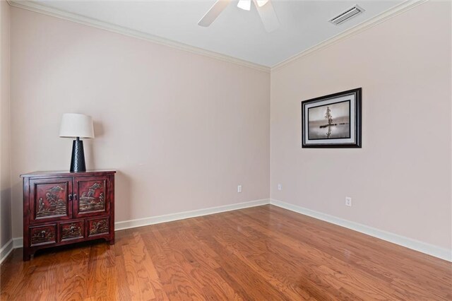 spare room featuring visible vents, crown molding, baseboards, and wood finished floors