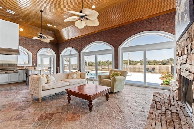 living area featuring visible vents, brick wall, wood ceiling, a fireplace, and high vaulted ceiling