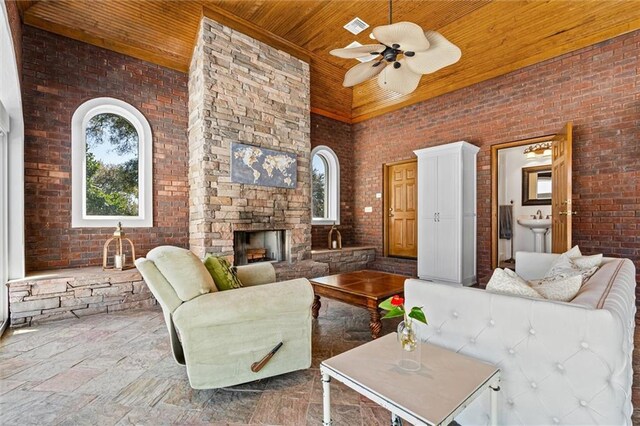 living room with visible vents, brick wall, a high ceiling, an outdoor stone fireplace, and wood ceiling