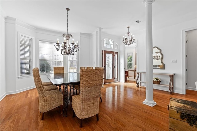 dining area with wood finished floors, an inviting chandelier, a healthy amount of sunlight, and ornate columns