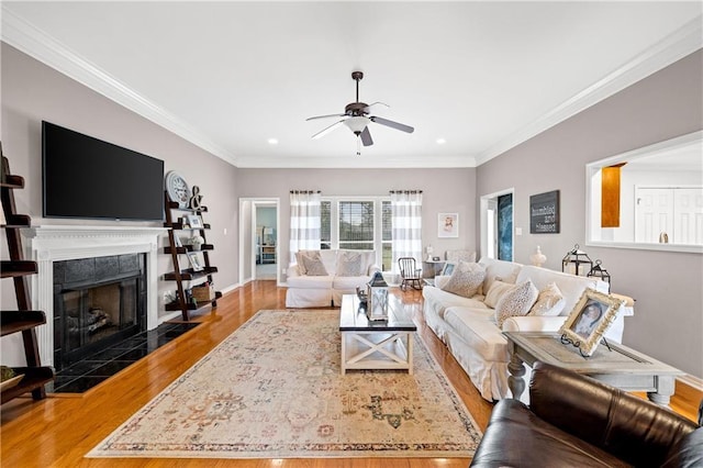 living room featuring a fireplace, hardwood / wood-style flooring, ceiling fan, and crown molding