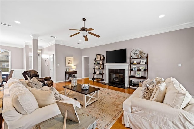 living room featuring ceiling fan, wood-type flooring, crown molding, and a tile fireplace