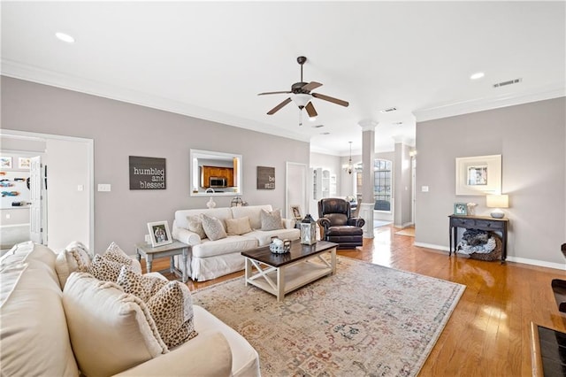 living room featuring wood-type flooring, ceiling fan with notable chandelier, and crown molding