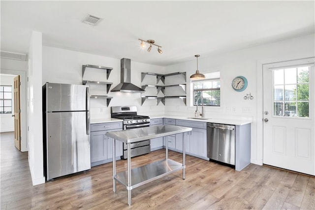 kitchen with sink, wall chimney exhaust hood, light hardwood / wood-style floors, decorative light fixtures, and appliances with stainless steel finishes