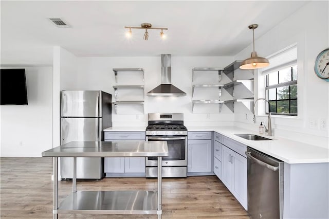 kitchen with hanging light fixtures, sink, wall chimney exhaust hood, appliances with stainless steel finishes, and light hardwood / wood-style floors