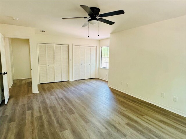 unfurnished bedroom with multiple closets, hardwood / wood-style floors, and ceiling fan