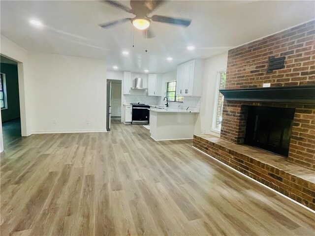 unfurnished living room featuring sink, a fireplace, ceiling fan, and light hardwood / wood-style flooring