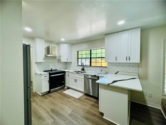 kitchen with dishwasher, light wood-type flooring, electric range, wall chimney range hood, and white cabinets