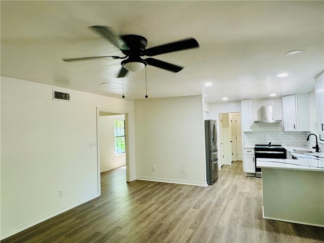 kitchen with appliances with stainless steel finishes, white cabinetry, wood-type flooring, and wall chimney range hood