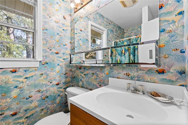 bathroom with toilet, vanity, and wallpapered walls