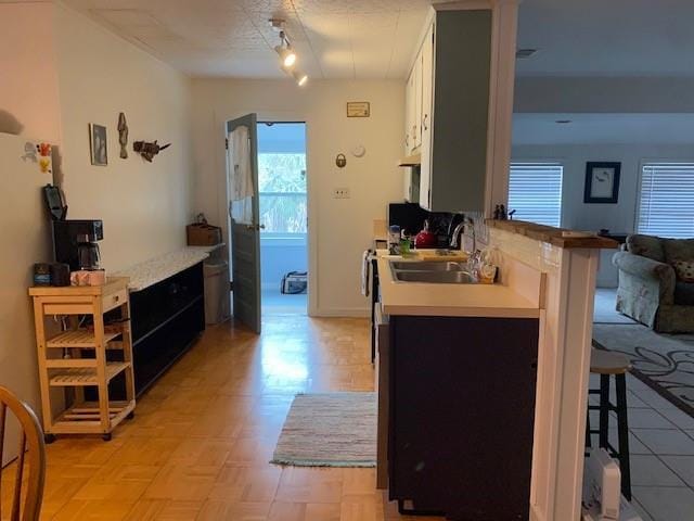 kitchen featuring a sink, light countertops, track lighting, white cabinets, and a kitchen breakfast bar