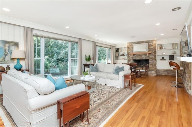 living room featuring built in shelves, light hardwood / wood-style floors, and a stone fireplace