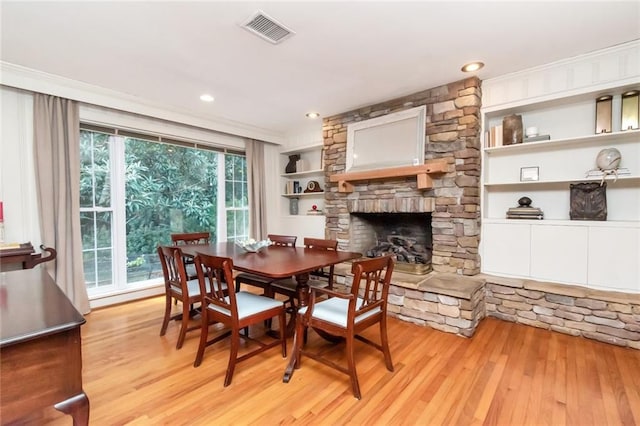 dining space featuring built in shelves, a stone fireplace, light wood-type flooring, and ornamental molding