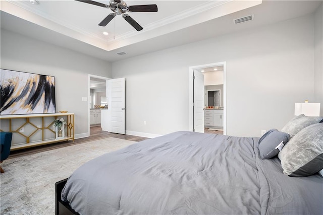 bedroom featuring ensuite bath, ornamental molding, a tray ceiling, ceiling fan, and hardwood / wood-style flooring