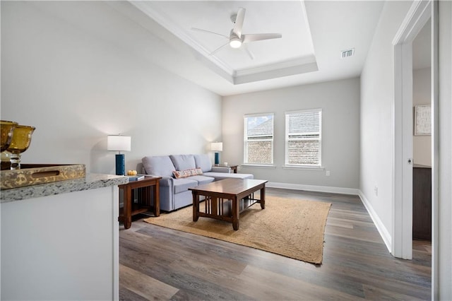 living room with a raised ceiling, ceiling fan, and dark hardwood / wood-style flooring