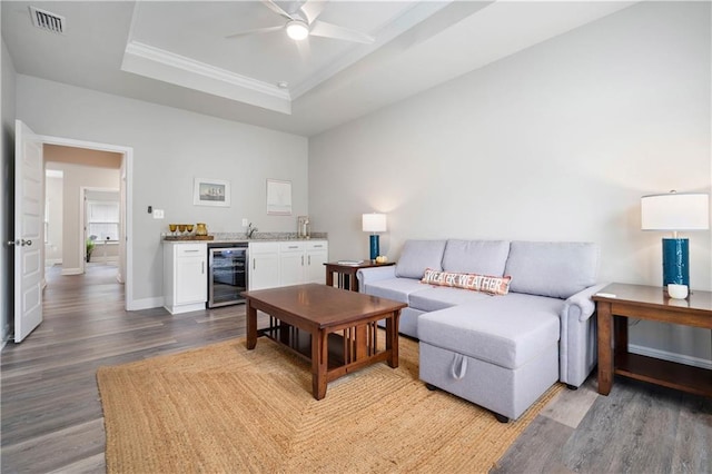 living room featuring wood-type flooring, a tray ceiling, beverage cooler, and ceiling fan