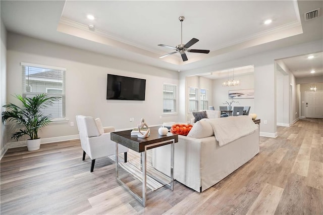 living room featuring a raised ceiling, crown molding, ceiling fan with notable chandelier, and light wood-type flooring