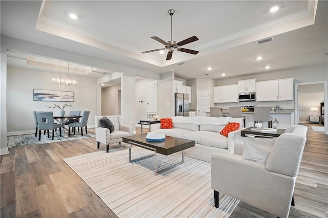 living room featuring a raised ceiling, ornamental molding, ceiling fan with notable chandelier, and light wood-type flooring