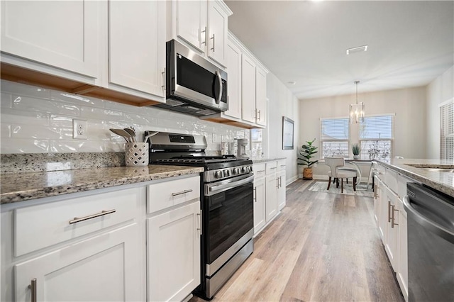 kitchen with hanging light fixtures, light stone counters, light hardwood / wood-style floors, white cabinets, and appliances with stainless steel finishes