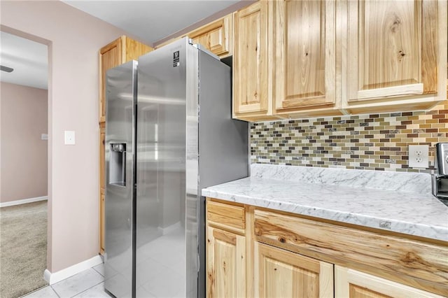 kitchen with light brown cabinetry, light tile patterned flooring, baseboards, backsplash, and stainless steel refrigerator with ice dispenser