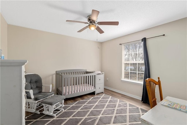 bedroom with wood-type flooring, a crib, and ceiling fan