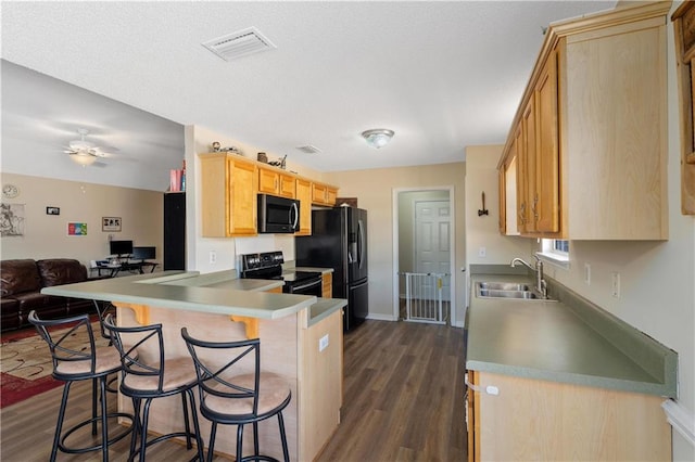 kitchen featuring black appliances, sink, kitchen peninsula, dark wood-type flooring, and a breakfast bar