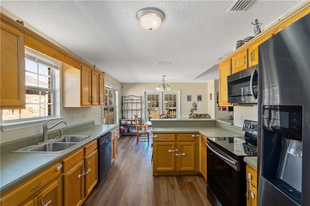 kitchen with kitchen peninsula, black appliances, dark wood-type flooring, pendant lighting, and sink