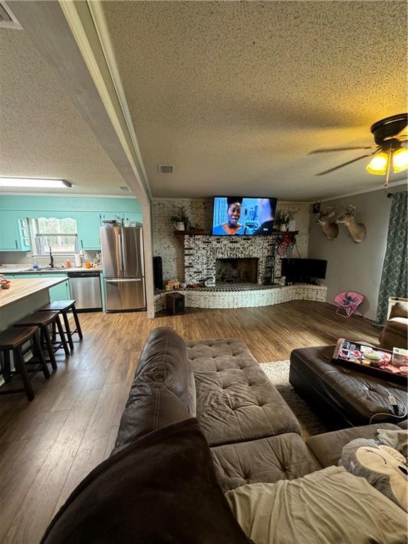 living room featuring ceiling fan, a fireplace, hardwood / wood-style floors, and a textured ceiling