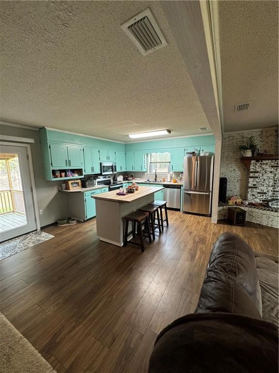 kitchen with appliances with stainless steel finishes, dark hardwood / wood-style flooring, a kitchen island, and a textured ceiling