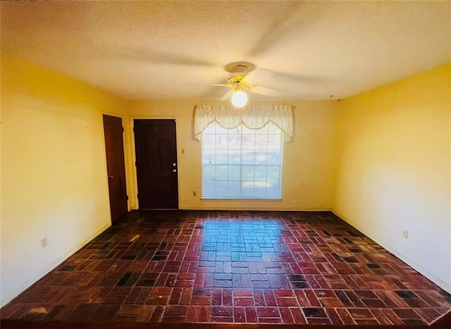 empty room featuring ceiling fan, a textured ceiling, brick floor, and baseboards