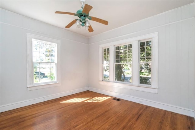 empty room with wood walls, wood-type flooring, and ceiling fan