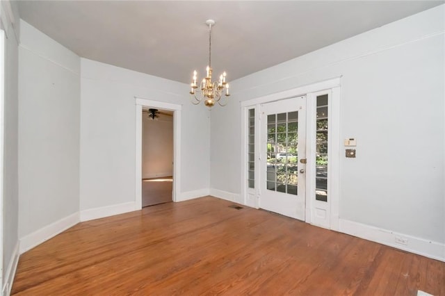 spare room with wood-type flooring and ceiling fan with notable chandelier