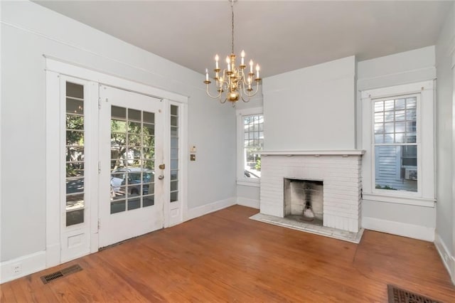 unfurnished living room with a brick fireplace, hardwood / wood-style flooring, an inviting chandelier, and plenty of natural light