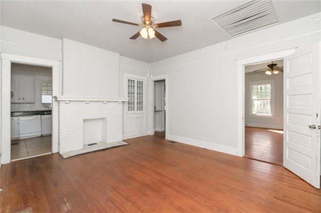 unfurnished living room with ceiling fan, sink, a fireplace, and hardwood / wood-style floors