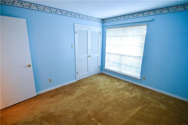 unfurnished bedroom featuring a closet, baseboards, multiple windows, and carpet flooring