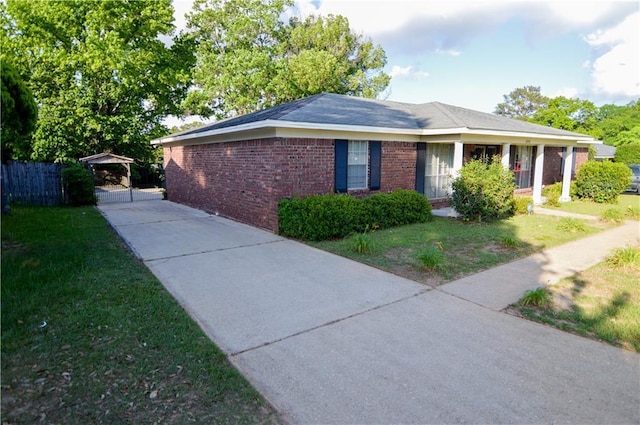 view of side of property with fence, brick siding, concrete driveway, a lawn, and a carport