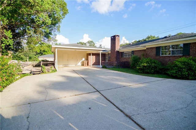 ranch-style home with brick siding, a carport, a chimney, and concrete driveway