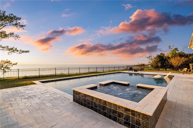 pool at dusk featuring a water view, a patio area, and an in ground hot tub