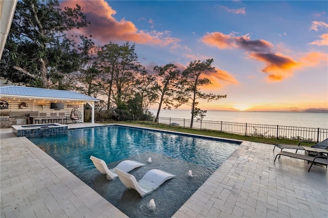 pool at dusk featuring a water view, a patio area, and area for grilling