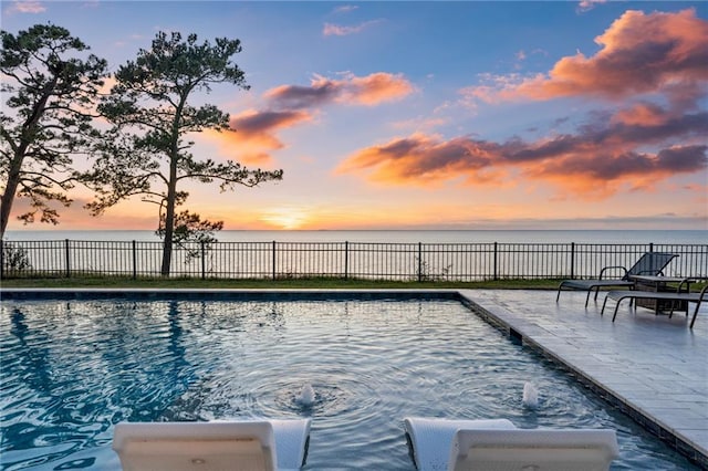 pool at dusk with a water view and a patio