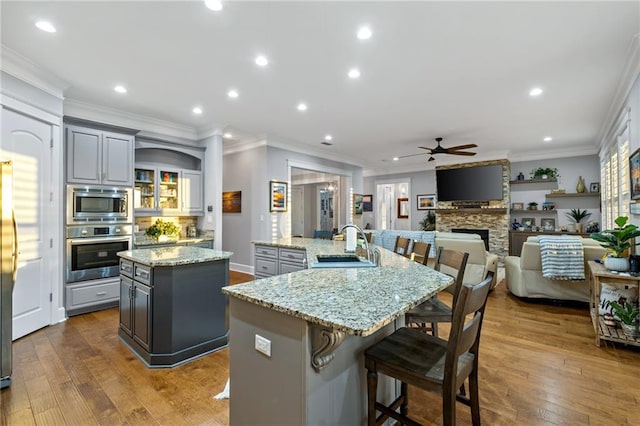 kitchen featuring a fireplace, wood-type flooring, an island with sink, stainless steel appliances, and sink