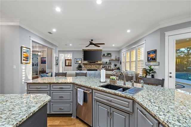 kitchen with sink, ceiling fan, a stone fireplace, stainless steel dishwasher, and light hardwood / wood-style floors