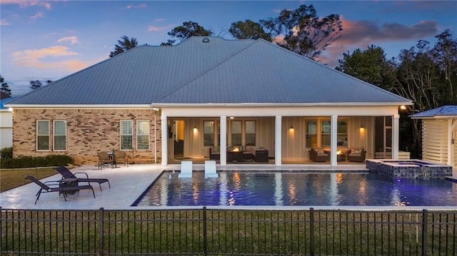 back house at dusk featuring a swimming pool with hot tub and a patio