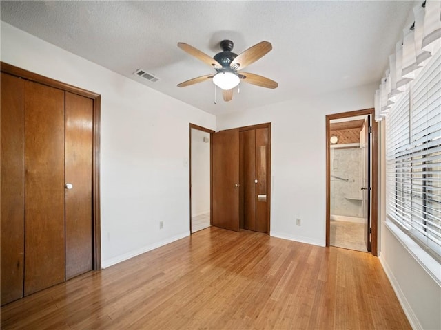 unfurnished bedroom with light wood-type flooring, ensuite bathroom, a textured ceiling, two closets, and ceiling fan