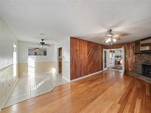 unfurnished living room featuring wood walls, a textured ceiling, and light hardwood / wood-style flooring